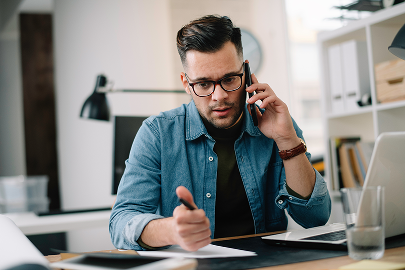 Homme au téléphone stylo à la main, devant son ordinateur 